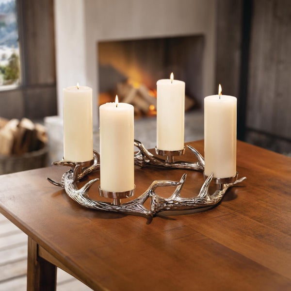 Adventskranz aus Metall in Geweihoptik mit vier brennenden Stumpenkerzen auf einem Holztisch vor einem Kamin.