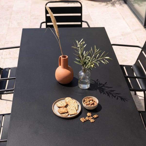 Moderner schwarzer Gartentisch mit passenden Stühlen auf einer hellen Terrasse, dekoriert mit Vasen, Gebäck und Nüssen.