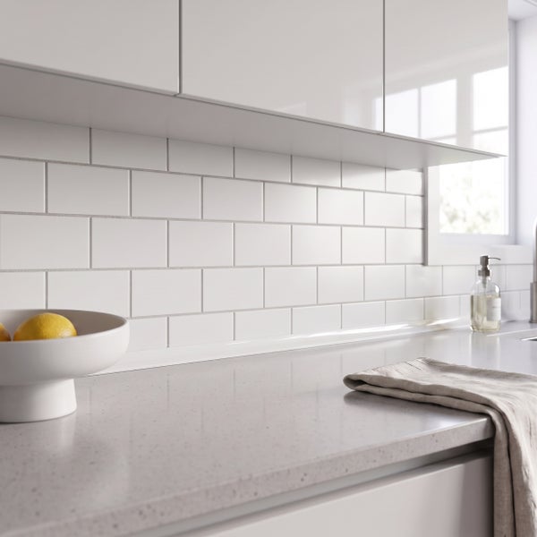 Moderne Küche mit weißen Wandfliesen im Ziegelverband, glatten Küchenfronten und einer Arbeitsplatte aus Steinoptik.