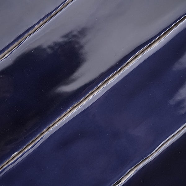 Dunkelblaue Wandfliese mit glänzender Oberfläche und unebener Kantenstruktur im Detail