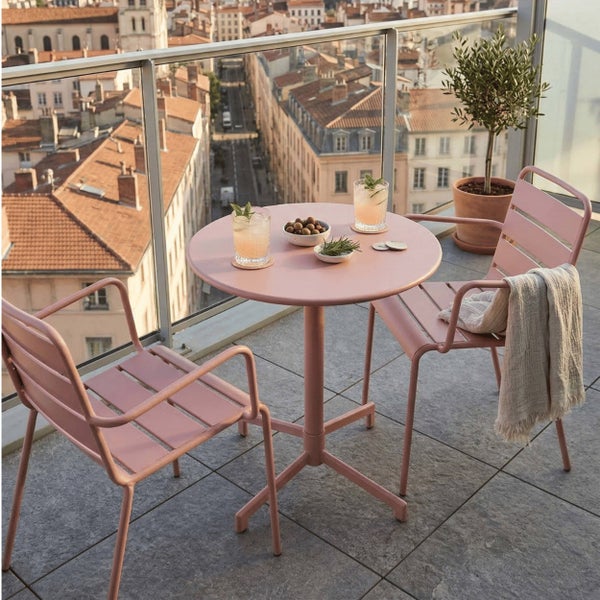 Moderner Balkontisch und zwei Stühle aus rosa Metall auf einem Balkon mit Blick über die Stadt.