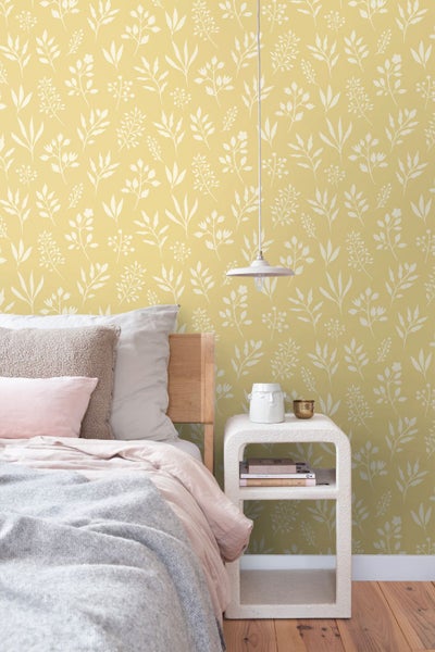 Vliestapete mit floralem Blättermuster in einem hellen Schlafzimmer mit Holzbett, weißem Beistelltisch und einer Hängelampe.