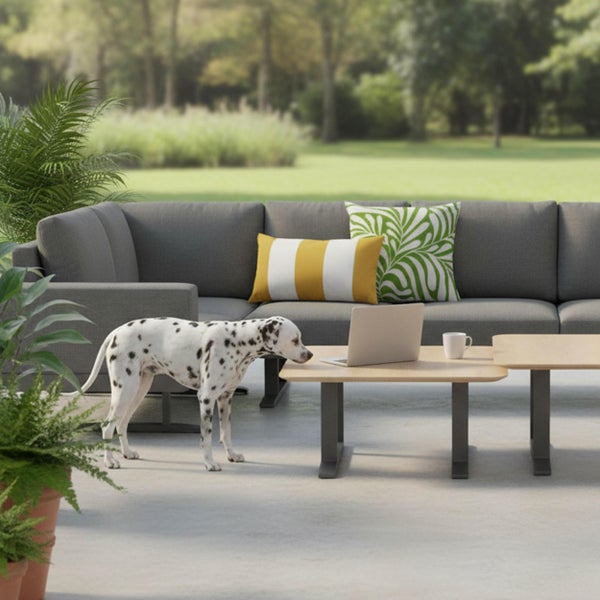 Graues Garten-Ecksofa auf einer Terrasse mit zwei Loungetischen aus Holz, einem Laptop, Zierkissen und einem Dalmatiner Hund.