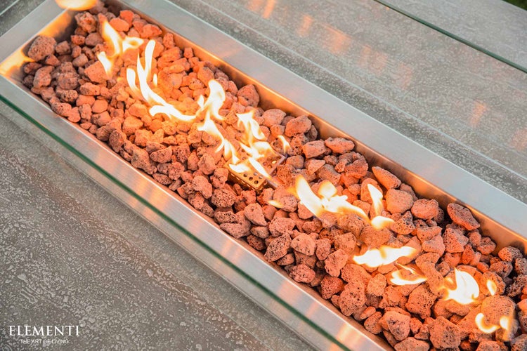 Elementi Logo. Gaskamin-Brenner aus Edelstahl mit Lavasteinen und brennenden Flammen hinter einem Glasschutz.
