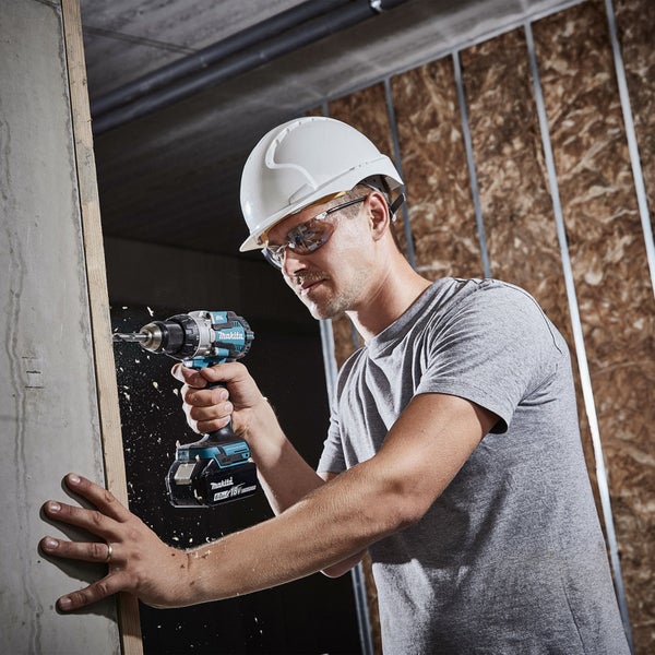 Handwerker bohrt mit einer Makita Bohrmaschine in eine Wand. Er trägt einen Schutzhelm und eine Schutzbrille.