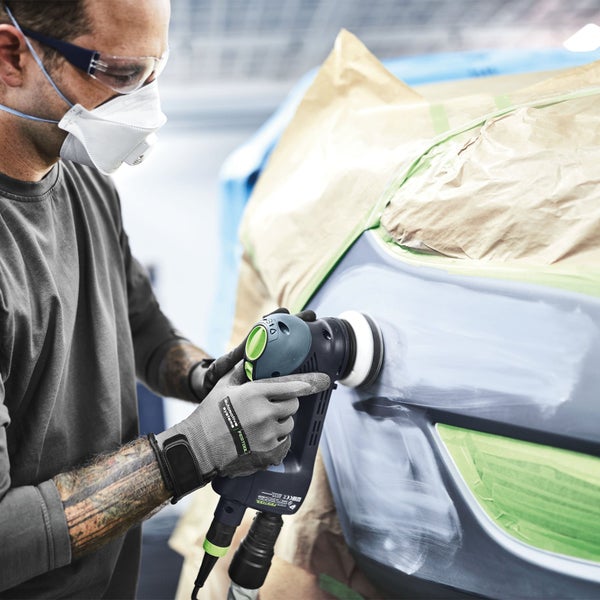 Ein Mann poliert mit einer Poliermaschine ein Auto, das mit Papier und Klebeband abgedeckt ist