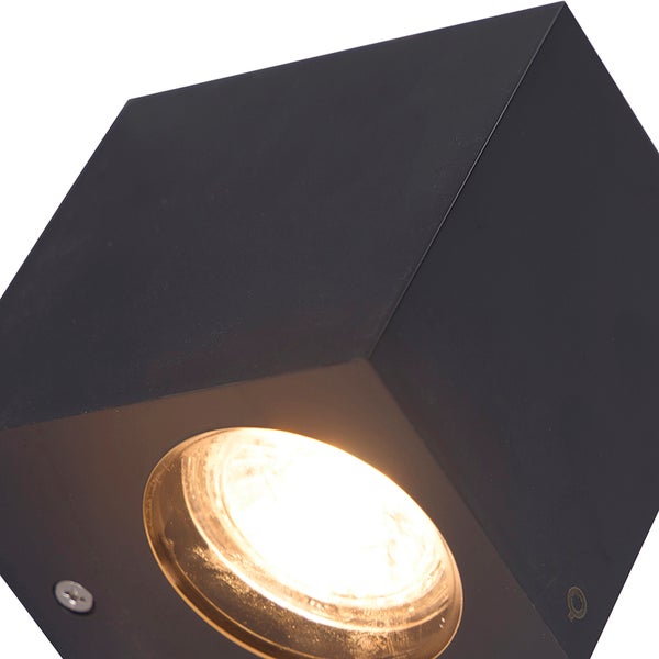 Schwarze würfelförmige Wandleuchte mit warmweißem Licht.