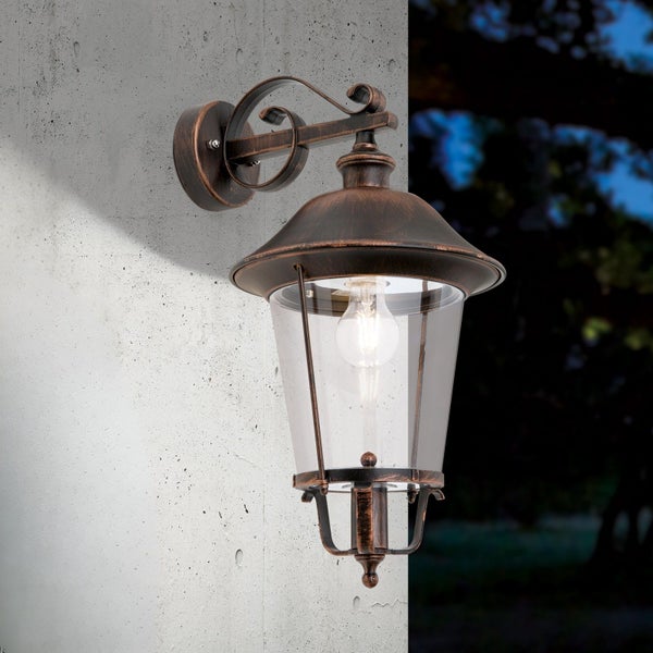 Klassische Außenwandleuchte in Laternenform aus Metall in Antik-Optik und klarem Glas, an einer Wand montiert.