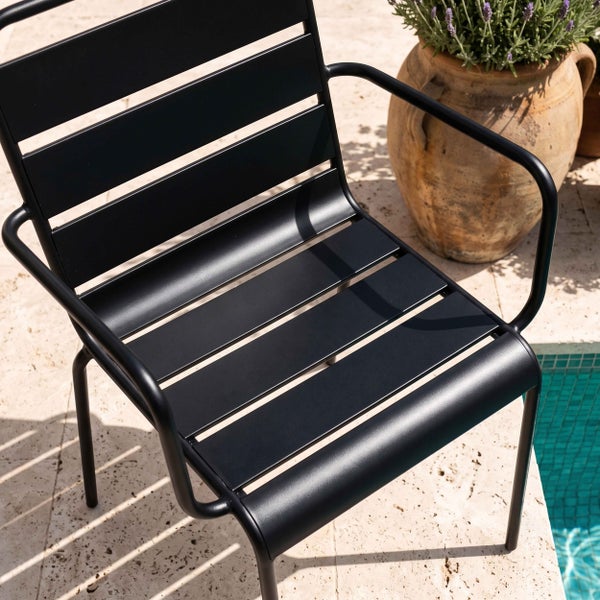 Moderner schwarzer Gartenstuhl aus Metall mit Latten und Armlehnen auf einer Terrasse neben einem Pool.