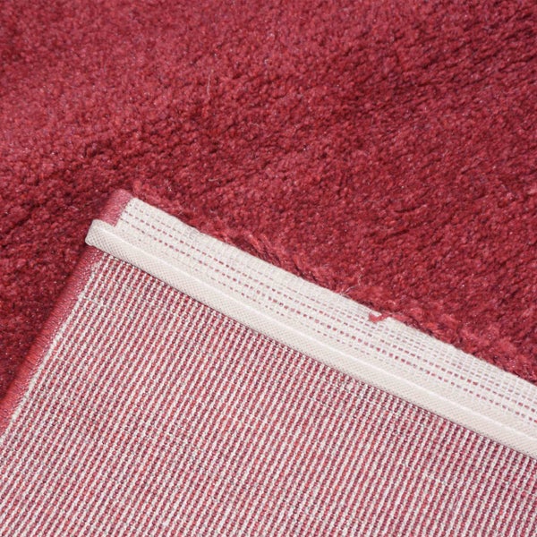 Nahaufnahme eines roten Plüschteppichs mit sichtbarer Florstruktur und gewebter Rückseite sowie eingefasster Kante.