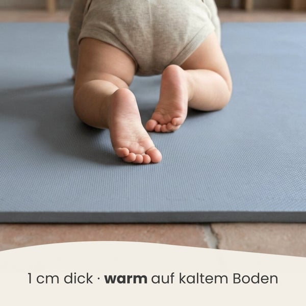 Baby krabbelt auf einer 1 Zentimeter dicken, strukturierten Spielmatte auf einem kalten Fliesenboden.