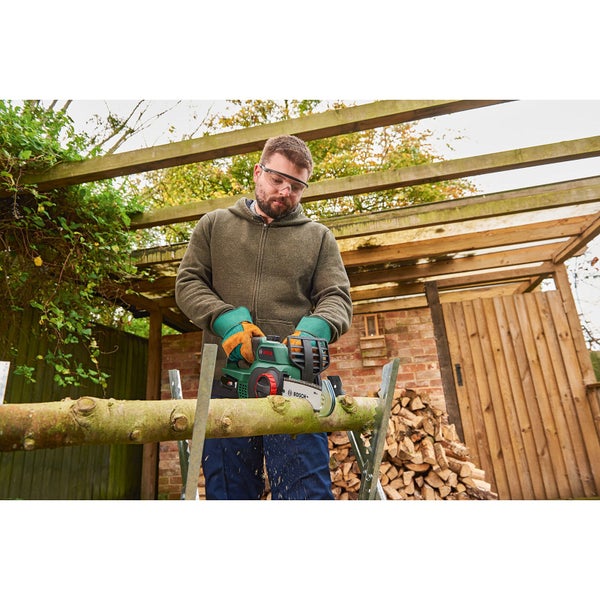 Mann sägt Holzscheit mit Akku-Kettensäge im Garten