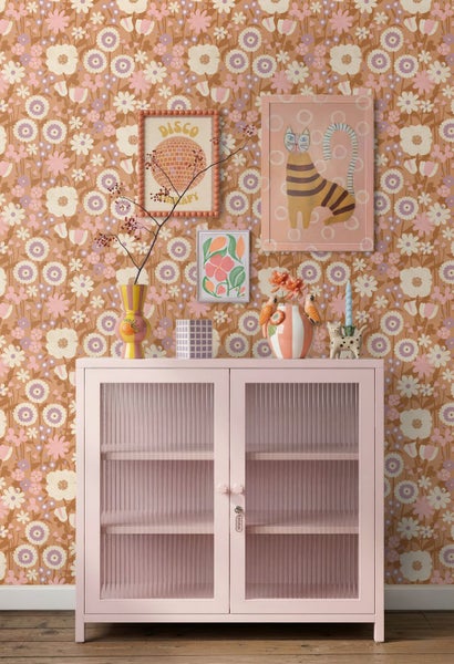 Rosa Vitrine mit geriffeltem Glas vor einer gemusterten Blumentapete im Retro-Stil mit dekorativen Accessoires.