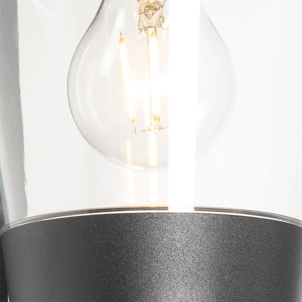 Nahaufnahme einer Außenleuchte mit klarem Glasschirm und sichtbarem LED-Filament-Leuchtmittel über einem dunklen Sockel.