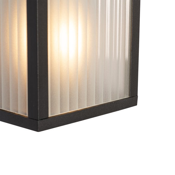Nahaufnahme einer Außenwandleuchte mit schwarzem Metallrahmen und geriffeltem mattiertem Glas mit warmem Lichtschein.
