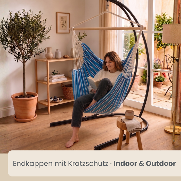 Eine Frau sitzt in einem blau gestreiften Hängesessel mit Holzstab in einem hellen Wohnraum mit Terrassenzugang und kratzgeschützten Endkappen.