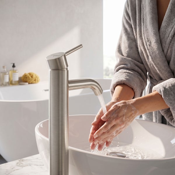 Hohe Einhebel-Waschtischarmatur in Edelstahl-Optik über einem weißen Aufsatzbecken in einem hellen Badezimmer während des Händewaschens.