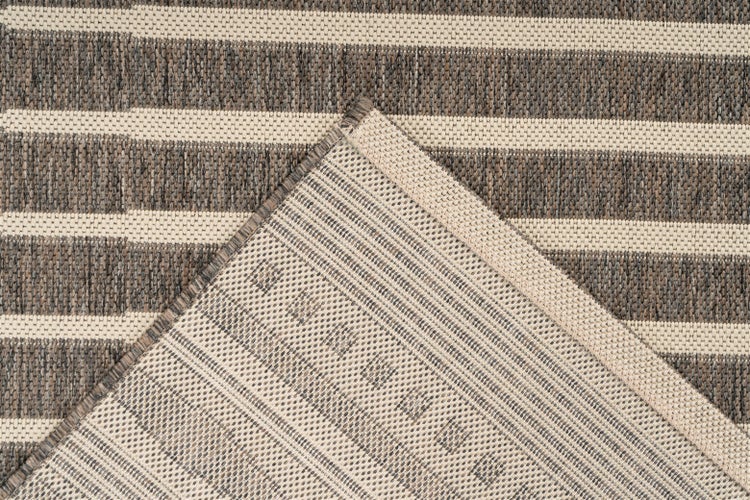 Detailansicht eines gestreiften Webteppichs mit umgeknickter Ecke zur Ansicht der Rückseite.