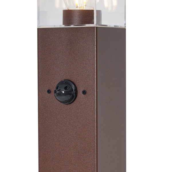 Nahaufnahme einer rostfarbenen Außenstandleuchte mit integriertem Bewegungsmelder und transparentem Aufsatz.