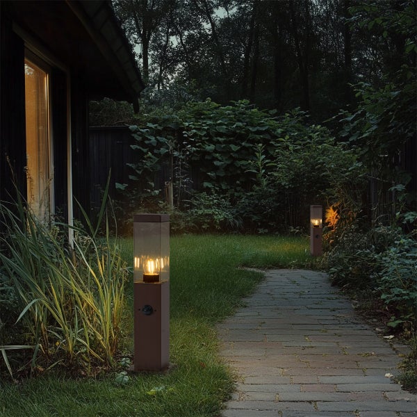 Zwei moderne, rechteckige Außen-Stehleuchten mit warmem LED-Licht beleuchten einen Gartenweg aus Stein bei Nacht inmitten grüner Pflanzen.