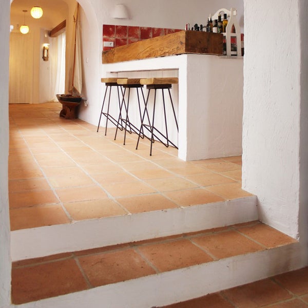 Rustikale Innenraumgestaltung mit Terrakotta Fliesen auf Boden und Treppe, einer Bar mit Holztresen und Barhockern in einem hellen Raum.