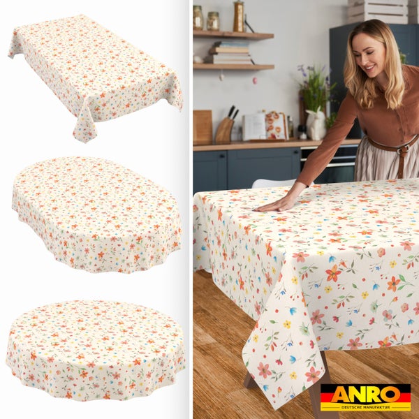 Tischdecke mit Blumenmuster in rechteckiger, ovaler und runder Form. Eine Frau legt die Decke in einer hellen Küche auf einen Tisch. ANRO Deutsche Manufaktur Logo.
