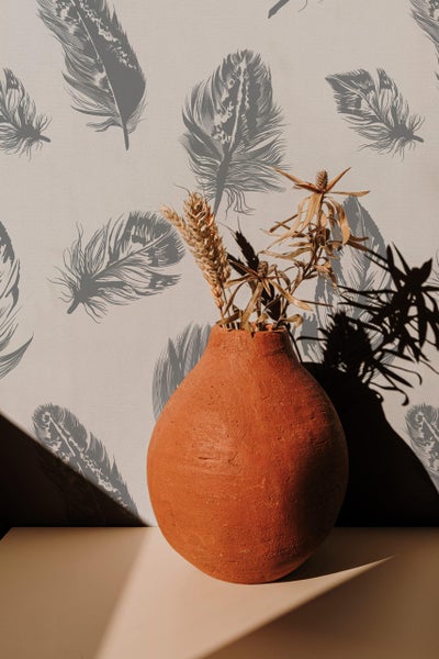 Terrakotta Vase mit getrockneten Getreidehalmen vor Tapete mit Feder Muster