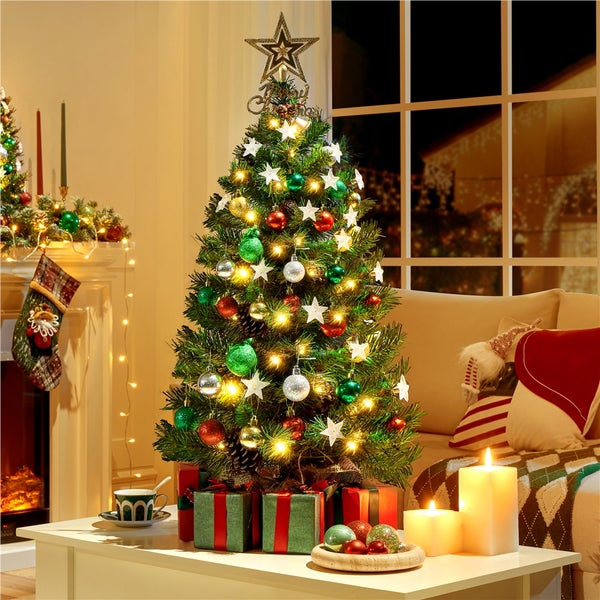 Festlich geschmückter Weihnachtsbaum mit Sternspitze, Kugeln, Sternen und Geschenken im gemütlichen Wohnzimmer.