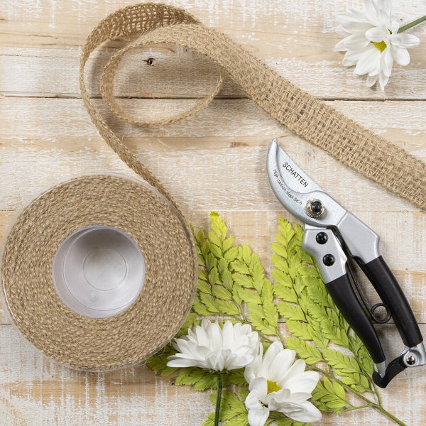 Juteband auf Rolle, Gartenschere der Marke Schatten und weiße Blumen auf Holzuntergrund.