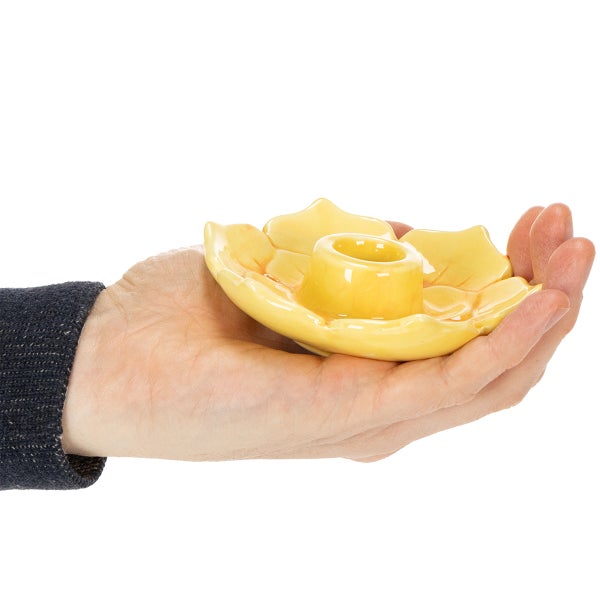 Gelber Kerzenhalter in Blütenform auf einer Hand