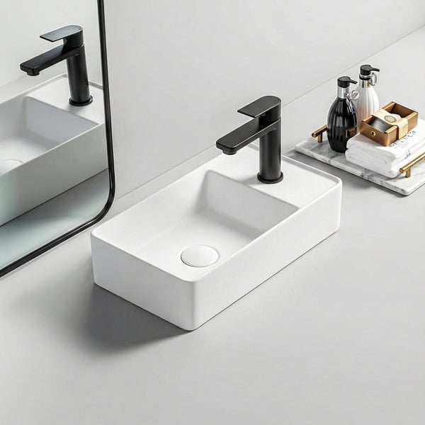Modernes rechteckiges Aufsatzwaschbecken mit schwarzer Armatur, Spiegelung im Hintergrund und Badaccessoires.