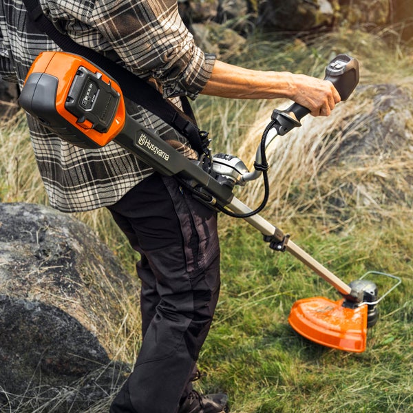 Eine Person benutzt einen Akku-Rasentrimmer der Marke Husqvarna im Garten.