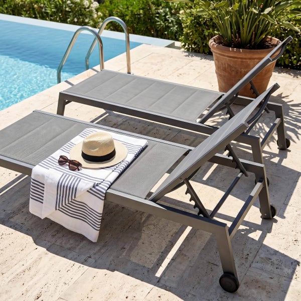 Zwei Gartenliegen aus Metall und Textilgewebe mit verstellbarer Rückenlehne und Rollen auf einer hellen Terrasse am Pool.