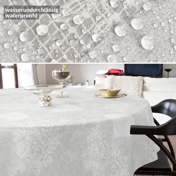 Runde Tischdecke mit Blumenmuster, wasserabweisend. Detailaufnahme mit Wassertropfen und Anwendungsbeispiel auf einem Tisch im Wohnzimmer.