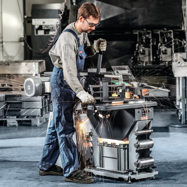 Handwerker in Arbeitskleidung bedient eine professionelle Metall-Bandschleifmaschine in einer Werkstatt, Funkenflug bei der Bearbeitung.