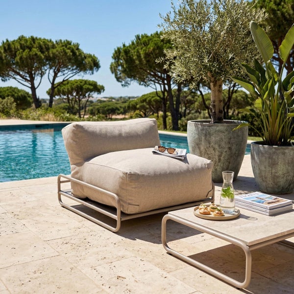 Moderner Garten-Loungesessel mit Metallgestell und hellem Polster neben einem passenden Beistelltisch an einem Pool auf einer hellen Steinterrasse.