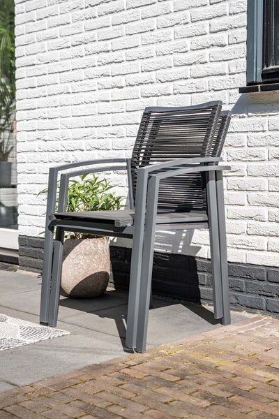 Stapelbarer Gartenstuhl mit Metallrahmen und Seilbespannung auf einer Terrasse vor einer Backsteinwand.