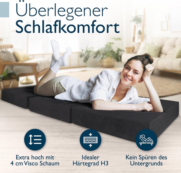 Frau liegt lächelnd auf einer schwarzen faltbaren Gästematratze aus Visco-Schaum mit Härtegrad H3 in einem hellen Wohnzimmer.