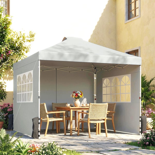 Grauer Faltpavillon mit Seitenwänden und bogenförmigen Fenstern, auf einer Terrasse mit Holz-Gartentisch und Flechtstühlen.