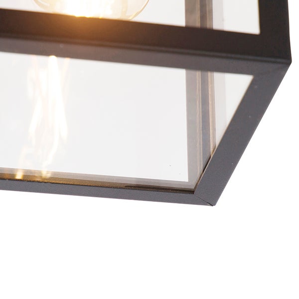 Nahaufnahme einer Lampe mit schwarzem Metallrahmen, Glaseinsätzen und sichtbarem Leuchtmittel.