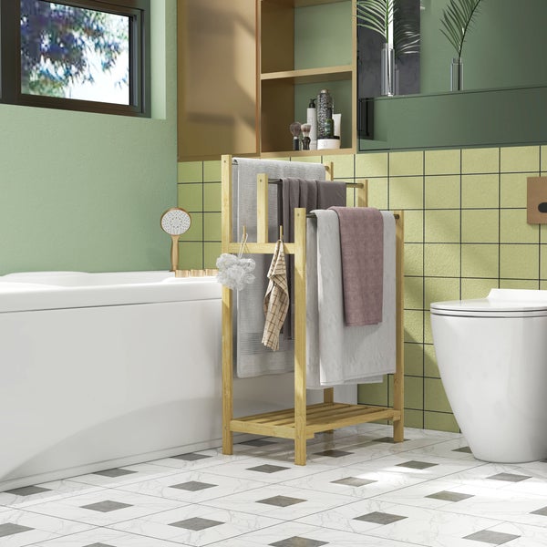 Freistehender Handtuchständer aus Bambus mit Handtüchern im hellen Badezimmer mit Badewanne, Toilette, grünen Fliesen und kariertem Boden.