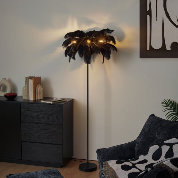 Schwarze Stehlampe in Palmenform mit Straußenfedern in einem modern eingerichteten Wohnzimmer neben einer dunklen Kommode.