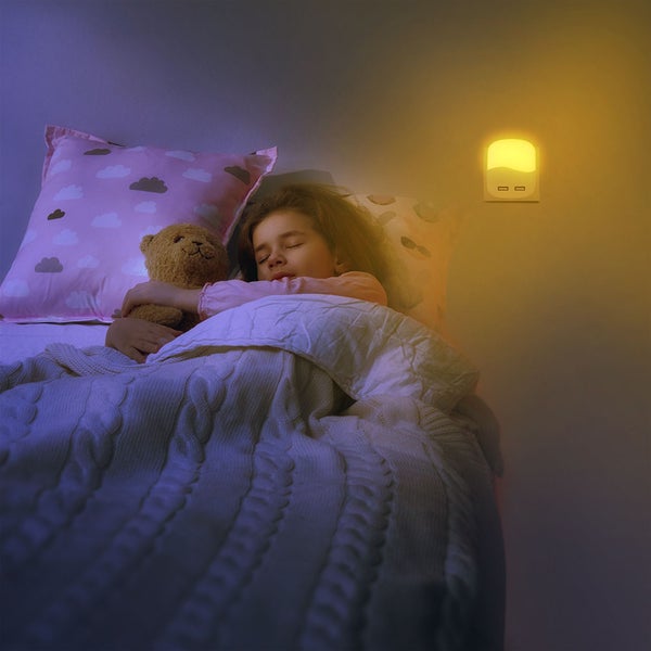 Mädchen schläft mit Teddybär im Bett unter einem Nachtlicht