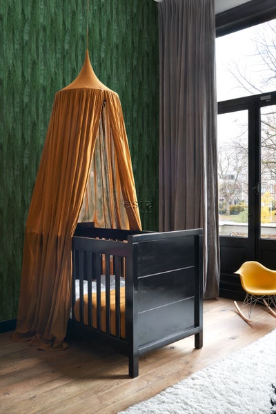 Kinderzimmer mit Gitterbett und Baldachin sowie gemusterter Tapete