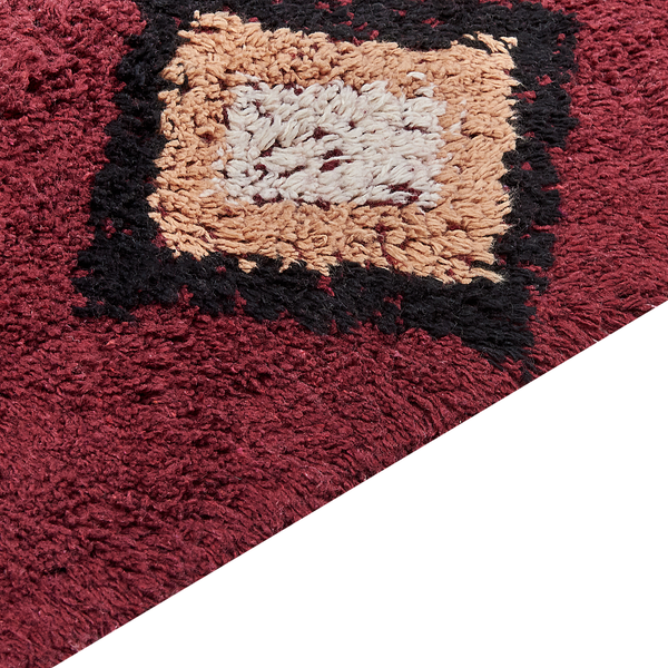 Nahaufnahme einer flauschigen Badematte mit Hochflor in Weinrot, Schwarz und Beige mit geometrischem Muster.