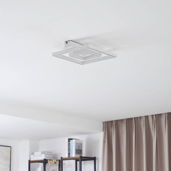 Moderne geometrische LED-Deckenleuchte mit Quadraten an einer weißen Decke in einem hellen, modern eingerichteten Raum.