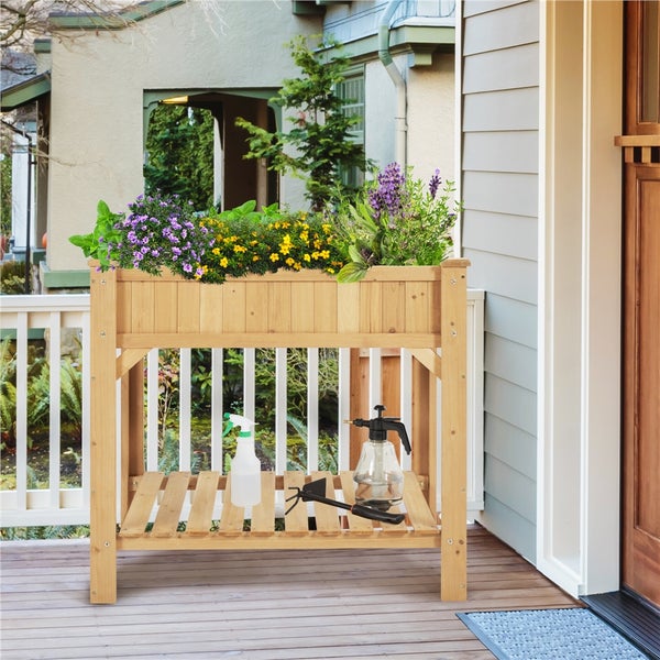 Hochbeet aus Holz mit Pflanzen und Gartenzubehör auf einer Terrasse