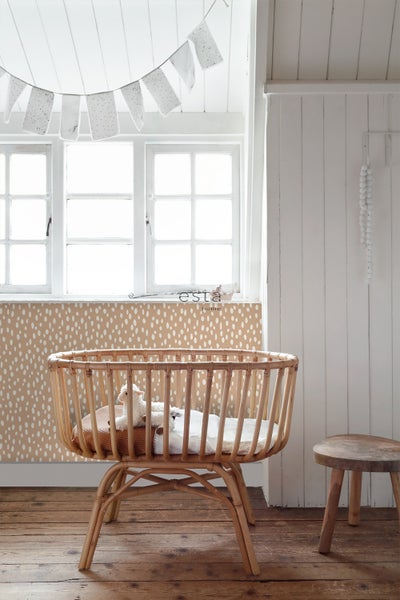 Kinderzimmer mit einem Kinderbett aus Rattan, einer Fensterdekoration und einer Tapete mit Punktmuster.
