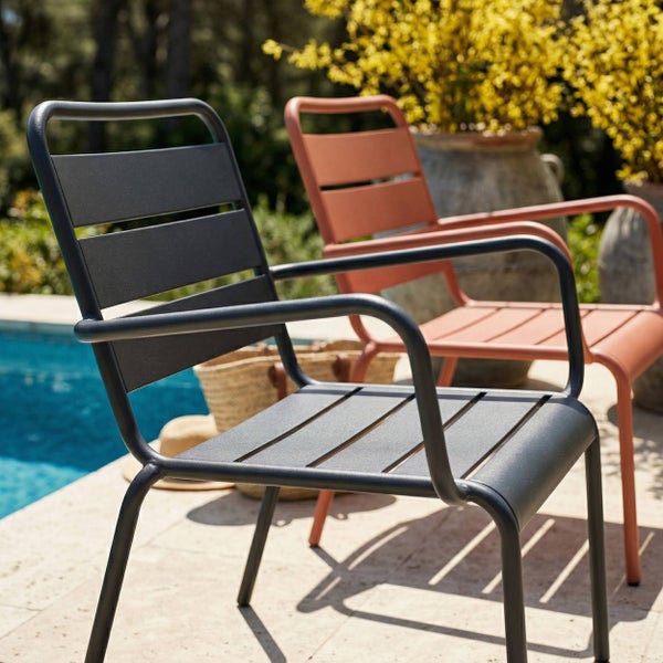 Moderne Gartenstühle aus Metall mit Latten und Armlehnen auf einer Steinterrasse an einem Swimmingpool.