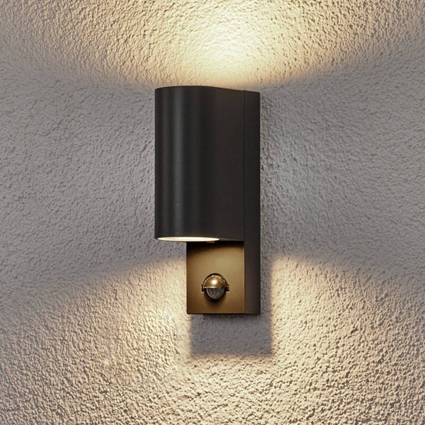 Außenwandleuchte mit integriertem Bewegungsmelder und Lichtaustritt nach oben und unten an einer strukturierten Wand.